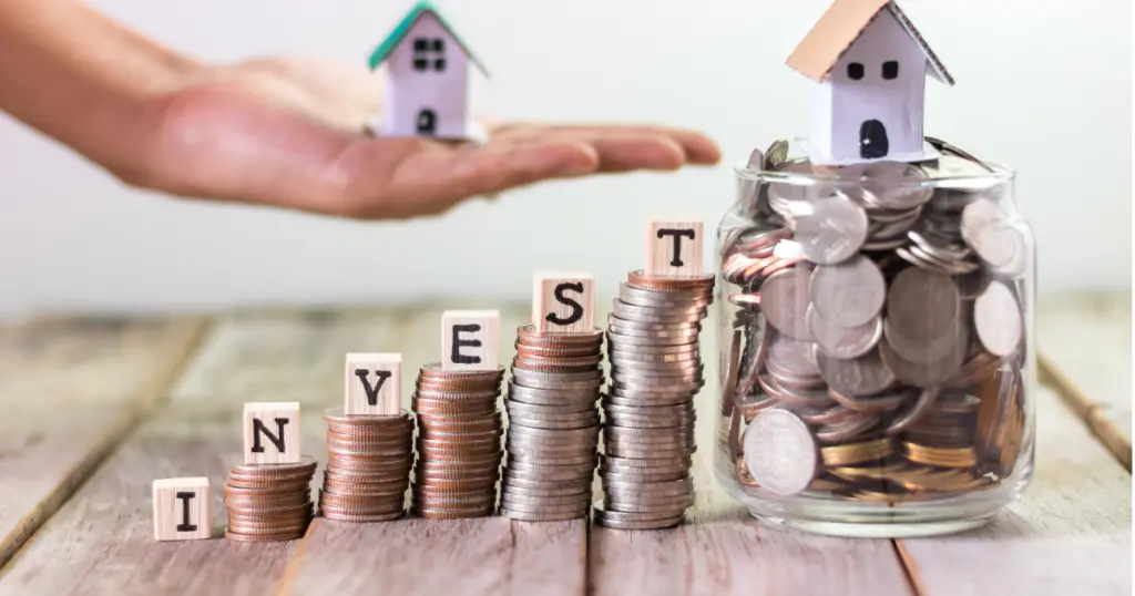 Stack of coins with blocks on top spelling out "invest" with a house on top of a jar filled with coins