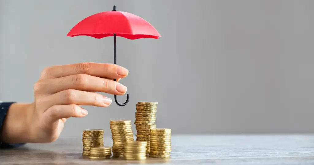 Hand holding a tiny umbrella over a stack of coins