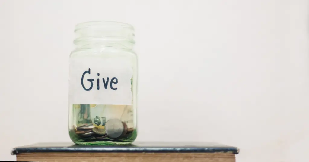 Clear glass jar wrapped with a label that says give and money inside