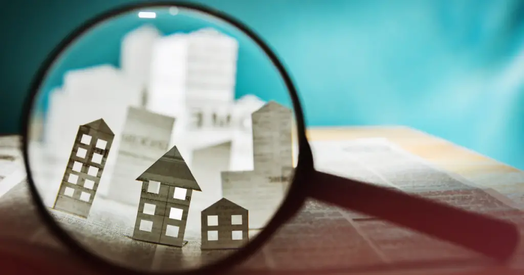 Looking through a magnifying glass at houses cut out of paper