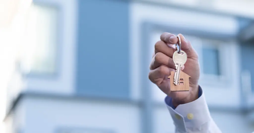 Hand holding keys in front of a house