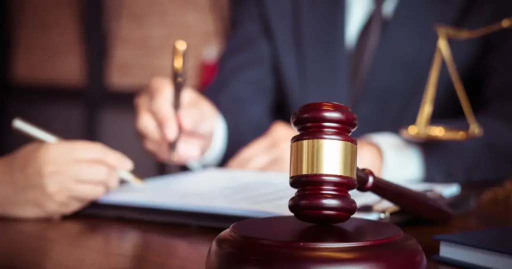 Person wearing a suit writing on a piece of paper with a gavel in foreground