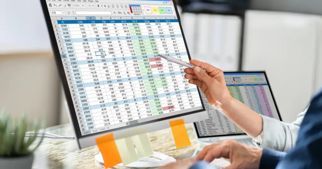 Person pointing a pencil at a computer monitor displaying a spreadsheet.