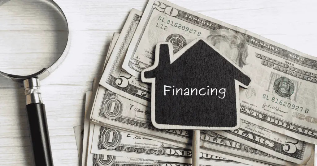 Financing written on a small house logo on top of a stack of money and next to magnifying glass