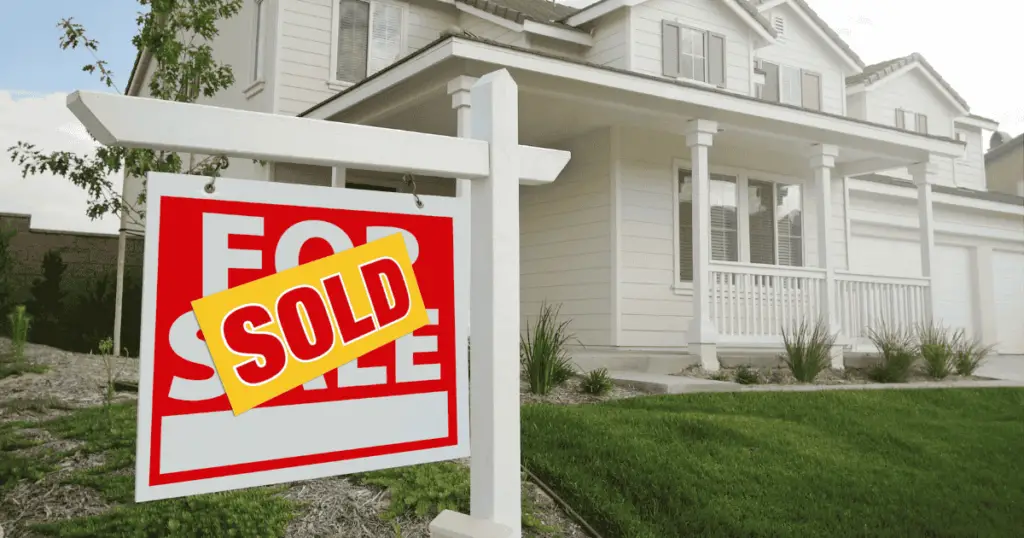 For sale sign with a sold sticker on top in front of a home